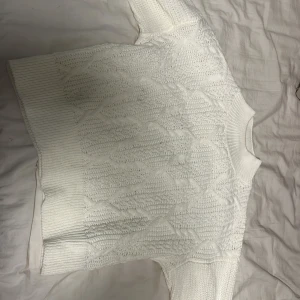 Vit stickad tröja - Säljer en mysig vit stickad tröja med ett fint kabelstickat mönster. Tröjan har långa ärmar och ribbstickade muddar vid ärmslut och nederkant. Perfekt för kyliga dagar!