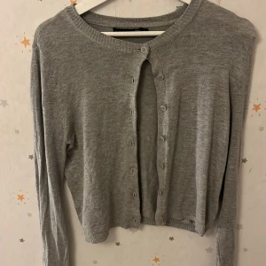 Grå kofta från 157 - Säljer en stilren grå kofta från 157. Den har långa ärmar och knappar framtill. Perfekt för lager-på-lager och passar till många olika outfits.