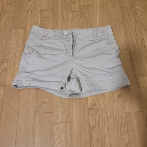 Beige shorts från H&M - Säljer ett par stilrena beige shorts från H&M. De har dekorativa knappar på sidorna. Perfekta för varma sommardagar!