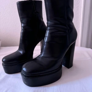Svarta platåstövletter - Snygga svarta platåstövletter med hög klack och dragkedja. Tillverkade i skinn för en stilren look. Perfekta för att höja din outfit till nästa nivå.