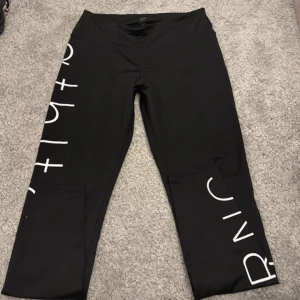 Svarta leggings med tryck - Snygga svarta leggings med vitt tryck längs benen. Perfekta för en stilren och bekväm look. Passar bra till både träning och vardag.