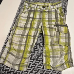 Rutig shorts med dragkedja - Snygga rutiga shorts i grönt och vit och grå med praktisk dragkedja på sidan. Perfekta för sommarens äventyr med en loose passform och bekvämt material.