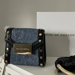 Jeansfärgad miniväska från Ideal of Sweden - Snygg och kompakt jeansfärgad miniväska från Ideal of Sweden med svarta detaljer och guldfärgad kedja. Köpt för 350 men säljer för 150, passar perfekt som student present😉.vid flera frågor gärna kontakta mig🥰🥰