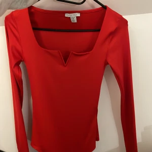 Röd långärmad topp från Missu - Snygg röd långärmad topp från Missu med en unik v-ringad design. Perfekt för att lägga till en färgklick i garderoben. Passar bra till både jeans och kjol.