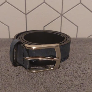 Blått skärp med silverfärgat spänne - Snyggt blått skärp. Skärpet har flera hål för justerbar passform. 105 cm långt Skick 9/10