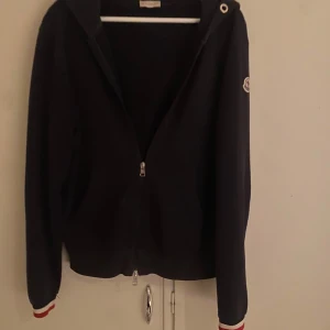 Moncler Maglia zip - Stilren Moncler zip tröja med broderad logga på ärmen. Säljer då den inte passar längre. Original snöret till luvan medföljer såklart.