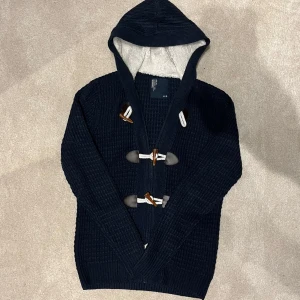 Cardigan med fodrad huva - Snygg mörkblå stickad hoodie med mysigt foder i luvan. Tröjan har dekorativa knappar framtill och ribbade muddar. Perfekt för kyliga dagar! Vid minsta fråga eller fundering hör av er🤝
