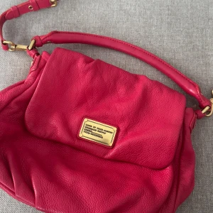 Röd axelväska i skinn - Snygg röd axelväska från Marc by Marc Jacobs i 100% skinn. Väskan har en justerbar axelrem och ett innerfoder med svartvitt mönster. Perfekt för att ge en färgklick till din outfit!