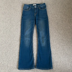 Blå jeans från Lindex - Snygga blå jeans från Lindex med bootcut-stil. De har en klassisk femficksdesign och en knapp med texten 'Detroit'. Perfekta för en avslappnad look.