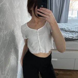Topp - Säljer en söt vit croppad topp med knappar framtill. Blusen har korta ärmar och en lätt ribbad struktur💓