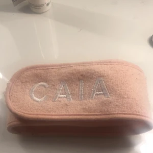Rosa diadem från CAIA - Säljer ett mjukt rosa diadem från CAIA med broderad logga. Perfekt för att hålla håret borta vid sminkning eller hudvård. Justerbart med kardborreband för bästa passform.