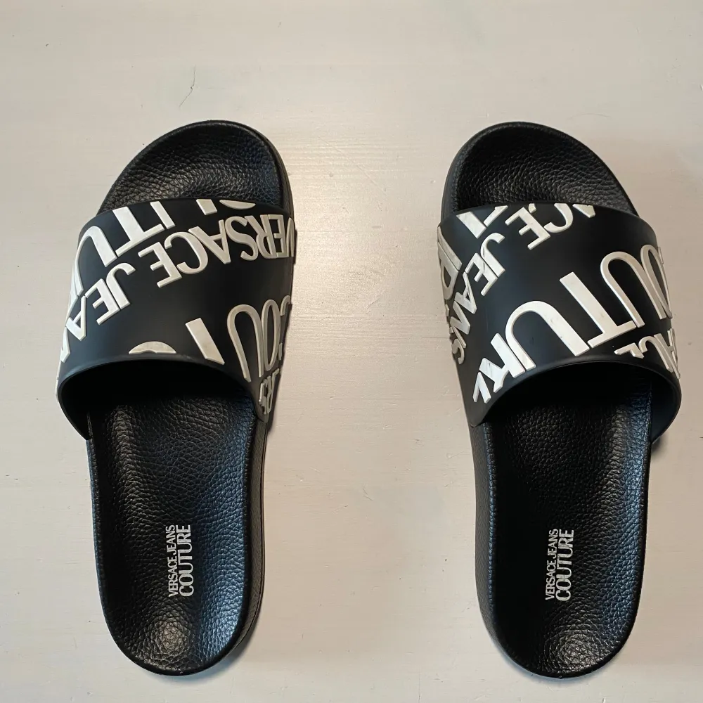 Snygga svarta sandaler med vit text på ovandelen. Sandalerna har en bekväm sula med mönstrad undersida för bra grepp. Perfekta för en avslappnad stil. Jag har storlek 43 och dom sitter lita tajt på mig. Jag gissar att dom är storlek 41-42. . Kengät.