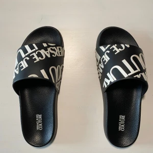 Svarta sandaler - Snygga svarta sandaler med vit text på ovandelen. Sandalerna har en bekväm sula med mönstrad undersida för bra grepp. Perfekta för en avslappnad stil. Jag har storlek 43 och dom sitter lita tajt på mig. Jag gissar att dom är storlek 41-42. 