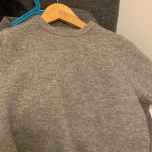 Grå stickad tröja från Zara - Säljer en stilren grå stickad tröja från Zara. Perfekt för kyligare dagar med sin mjuka och bekväma passform. Tröjan har långa ärmar och ribbade kanter vid ärmslut och nederkant. Ett måste i garderoben för en klassisk look. Kostade originellt 300