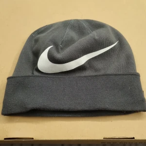 Nike mössa - Snygg grå mössa från Nike med det ikoniska vita swoosh-loggan framtill. Perfekt för kyliga dagar och ger en sportig touch till din outfit. Tillverkad i mjukt material för extra komfort.