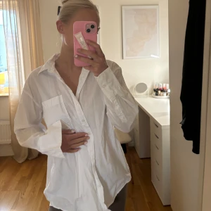 Vit skjorta - Säljer en klassisk vit skjorta med långa ärmar och knappar framtill. Perfekt för en stilren look. Skjortan har en normal passform och är tillverkad i ett lätt och bekvämt material.