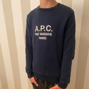 Mörkblå sweatshirt från A.P.C. - Snygg mörkblå sweatshirt från A.P.C. med texten 'RUE MADAME PARIS' på bröstet. Storlek: S Tillverkad i Portugal. Modellen är 176  
