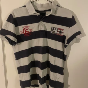 Randig pikétröja från Lexington - Säljer en klassisk randig pikétröja från Lexington i marinblått och vitt. Tröjan har korta ärmar och broderade detaljer på bröstet. Perfekt för en avslappnad stil.kan byta 