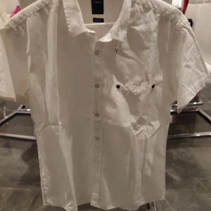 Vit kortärmad skjorta från Emilio - Säljer en stilren vit kortärmad skjorta från Emilio. Skjortan har knappar framtill och en liten bröstficka med knappdetalj. Perfekt för en avslappnad men ändå snygg look. 🕶️