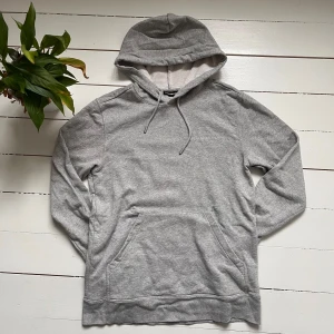 Grå hoodie från J.Lindeberg - Säljer en stilren grå hoodie från J.Lindeberg. Den har en klassisk design med dragsko i huvan och en broderad logga på bröstet. Perfekt för en avslappnad look.