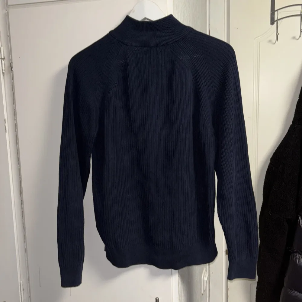 Säljer en stilren mörkblå stickad tröja från Gant med dragkedja vid halsen. Tröjan har långa ärmar och ett diskret broderat märke på bröstet. Perfekt för kyligare dagar. PRIS KAN DISKUTERAS!. Neuletakit & Villapaidat.
