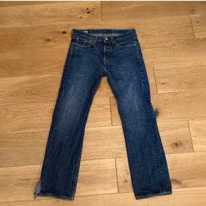 Blå jeans från Levi's - Säljer ett par klassiska blå jeans från Levi's med rak passform. De har en traditionell femficksdesign och knappgylf. Perfekta för en avslappnad stil. Liten defekt nedtill.