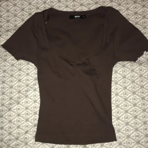 Brun ribbad topp från Bik Bok - Säljer en brun ribbad topp från Bik Bok i storlek XS. Toppen har en v-ringad design och korta ärmar, perfekt för en stilren look.