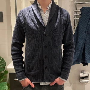 Mörkblå kofta från Hollister - Säljer en snygg mörkblå kofta från Hollister med knappar framtill och ribbade detaljer. Perfekt för festliga dagar men funkar även vardagligen med sin stickade design och långa ärmar. Koftan har en klassisk krage och två praktiska fickor. Storlek Small och väldigt bra skick.