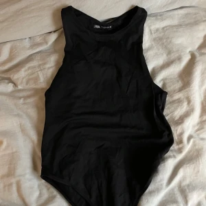Svart ärmlös bodysuit från Zara - Säljer en stilren svart bodysuit från Zara. Den är ärmlös och har en enkel design som passar perfekt för lager-på-lager eller som den är. Tillverkad i ett mjukt och bekvämt material.