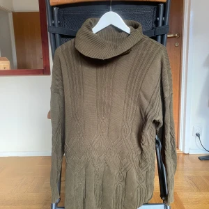 Olivgrön stickad polotröja från Kurt Kellermann - Säljer en olivgrön stickad polotröja från Kurt Kellermann. Tröjan har ett snyggt kabelstickat mönster och en hög polokrage. Den är låg och är även jättesnygg som kort klänning. Om man vill ha den som kofta funkar den absolut för en storlek M.