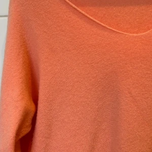 Stickad tröja i aprikos - Säljer en aprikos färgad tröja med lång ärm och v-ringad hals. Den är otroligt mjuk och nopprar inte av sig. Har denna i två färger till (vit och beige). Kan användas på båda sidor, beroende på om man gillar rak hals eller v ringad hals. Köpt på mitt tidigare jobb på västkusten, därav ingen märkning eller storlek. Men storleken ska va ”one size” 