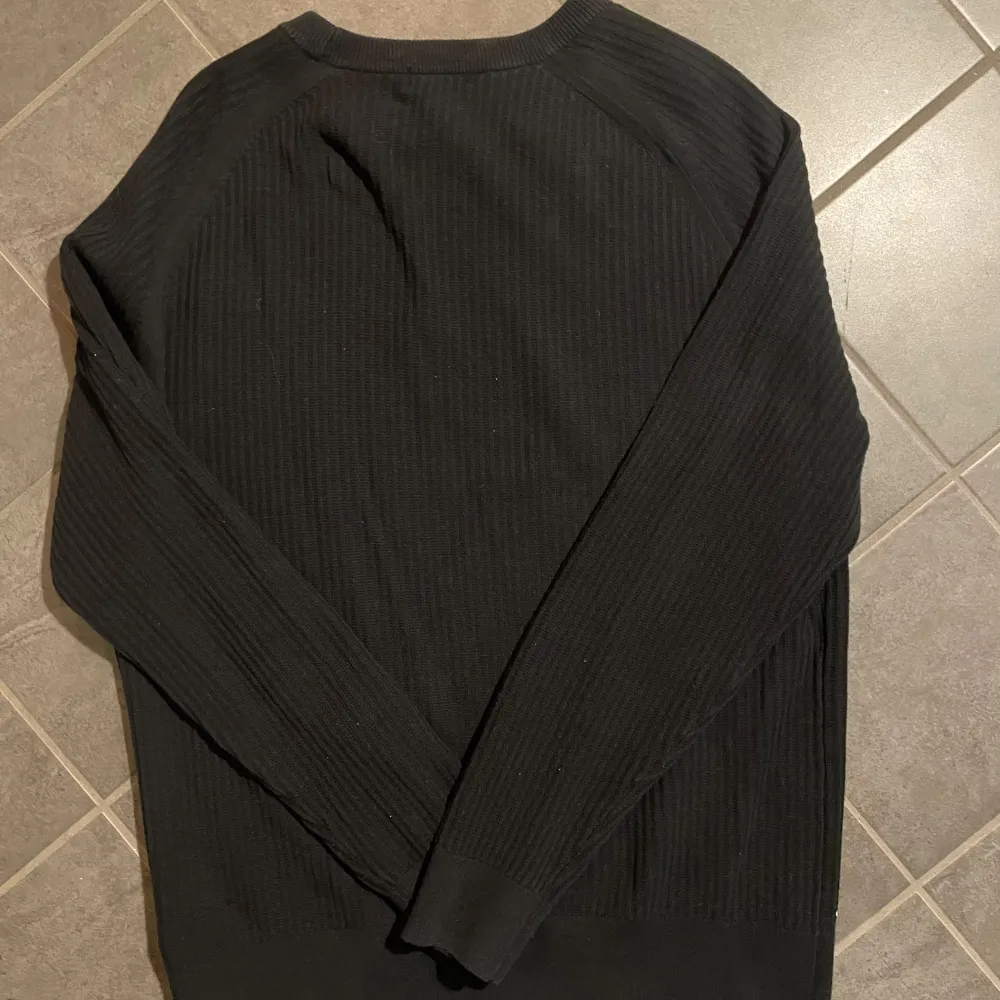 Säljer en stilren svart ribbad tröja från J.Lindeberg. Tröjan har långa ärmar och en klassisk rund halsringning. Perfekt för en minimalistisk look.. Neuletakit & Villapaidat.