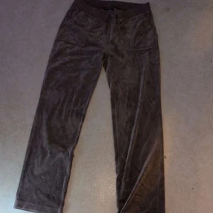Bruna byxor från Juicy Couture - Snygga bruna byxor från Juicy Couture i mjukt material. De har en bekväm passform med resår i midjan och fickor bak med knappar. Perfekta för en avslappnad stil. Dom två silver plattorna som ska vara på snörena har tyvärr gått av, annars är dom i jätte bra sikt💞