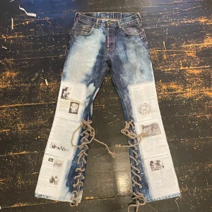 Unika jeans med tidningsmönster och snörning - Säljer ett par custom made coola jeans med tidningsmönster och snörning längs benen. De har en unik design med blekta partier och tryck av tidningsartiklar. Perfekta för dig som vill sticka ut!