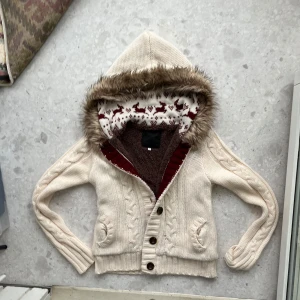 Tröj med päls från new look - Mysig beige stickad kofta med knappar och huva. Huvan har en fin pälsdetalj och insidan är mönstrad med renar. Perfekt för kyliga dagar.