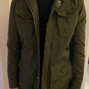 Grön jacka från J.Lindeberg - Snygg grön jacka från J.Lindeberg med dragkedja och knappar. Jackan har flera fickor, dubbel dragkedja. Perfekt för höst och vår.