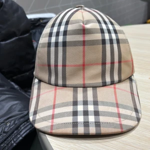 Rutig keps från Burberry - Snygg keps från Burberry med klassiskt rutigt mönster i beige, svart och rött. Justerbar passform med spänne bak och stilren design med Burberry-logga byter även mot lv mössa äkta 