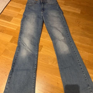 Blå jeans från Wrangler - Snygga blå jeans från Wrangler med en hög midja. De har en flare-stil som ger en trendig look. Jag har kortat ner benen lite då byxorna var för långa för mig. Så nu passar de mig perfekt i längden och jag är 162cm lång. Använd några gånger. Storleken är ursprungligen W26 L32, men är numera som en L30 :)