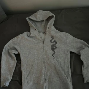 Grå hoodie med ormmotiv - Snygg grå hoodie med dragkedja och ett coolt ormmotiv på framsidan. Perfekt för en avslappnad stil. Den har en bekväm luva och långa ärmar. Pris går att diskutera!🤩