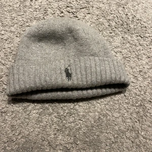 Grå mössa från Polo Ralph Lauren - Snygg grå mössa från Polo Ralph Lauren med ribbad kant och broderad logga. Perfekt för kyliga dagar.