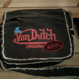 axelväska från Von Dutch - Intressekol på en sjukt cool Von Dutch Väska‼️skicka rimliga prisförslag. Köpt på en vintage butik för ett högt pris, har andvänt mycket och har tyvärr en tradig dragkedja men det går säkert ganska lätt att fixa om man vet vad man gör👌 några av fransarna har även rivigts upp men annars är väskan i bra skicka❤️ även en perfekt väska för skolan då den får plats med både en dator och mappar💕