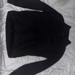 Svart grish tröja - Snygg svart tröja med quiltad detalj över bröstet och knappar vid halsen. Perfekt för kyligare dagar.