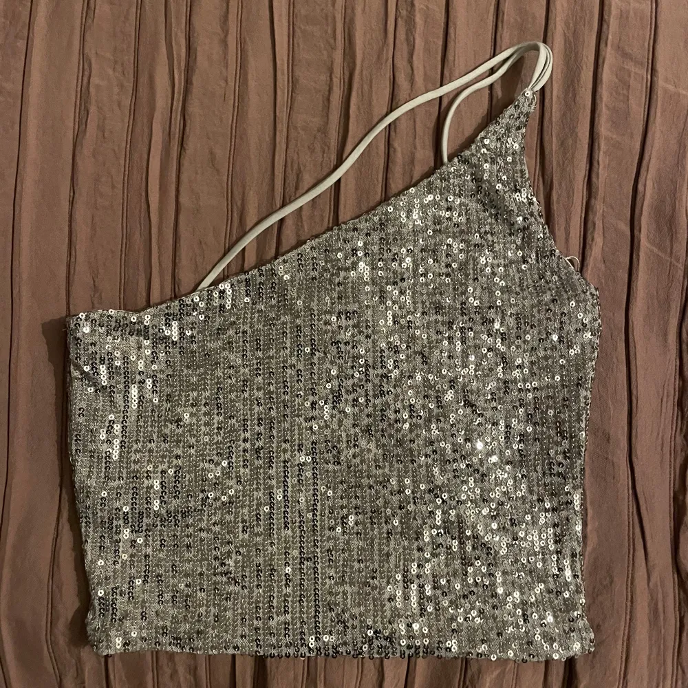 Snygg silverfärgad oneshoulder topp från Amisu, täckt med glittrande paljetter. Helt ny med prislapp💗. Yläosat.