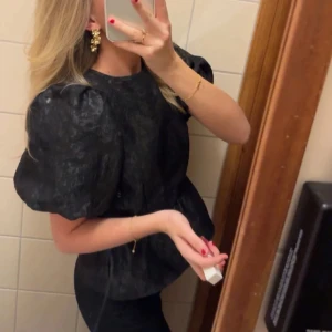Svart lyxig blus  - Elegant svart blus med puffiga kortärmar och knytning i ryggen. Storlek s