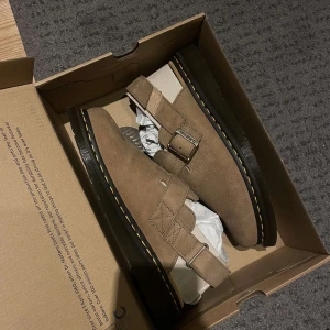 Bruna skor från Dr. Martens - Snygga bruna sandaler från Dr. Martens i mocka med dubbla spännen. Perfekta för en stilren look med den klassiska gula sömmen och robust sula.                     Säljer min killes helt nya dr martens jorge 11 i färgen ”savannah tan” sandfärgade/bruna.  Säljes pga går inte att retunera, beställde för länge sedan och skulle bli en julklapp men stlken var för stor. Han har 42,5 vanligtvis. Dessa i storlek 43.  Artikeln skickas i sin orginalkartong. Pris kan diskuteras.