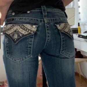 Blå jeans med dekorerade bakfickor från Miss Me - Snygga blå jeans från Miss Me med unika dekorerade bakfickor. Byxorna har en bootcut-stil och låg midja, vilket ger en trendig look. Perfekta för dig som vill sticka ut med detaljerade fickor och snygga knappar. Säljer pga att de är för stora i midjan. Köpta här på plick❤️ skriv ifall du har några frågor❤️ (tryck inte på köp nu utan att kontakta mig!!!)