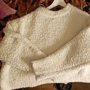 Vit fluffig tröja - Mysig vit tröja med fluffig textur. Perfekt för kyliga dagar med sin varma och bekväma design. Tröjan har långa ärmar och en rund halsringning.
