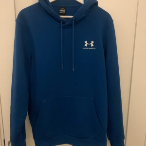 Blå hoodie från Under Armour - Säljer en snygg blå hoodie från Under Armour. Den har en klassisk design med en känguruficka och justerbar huva. Perfekt för en avslappnad stil eller träning. 🏋️‍♂️
