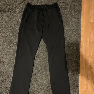 Hugo Boss mjukisbyxor  - Säljer ett par svarta mjukisbyxor från Boss med elastisk midja och snörning. Byxorna har en avslappnad passform och är perfekta för en bekväm stil. Diskret Boss-logga på sidan.