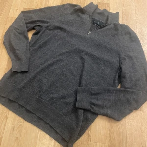 Grå merinoulltröja från Riley - Säljer en stilren grå tröja i merinoull från Riley. Tröjan har en dragkedja vid halsen och långa ärmar, perfekt för kyligare dagar. Den är mjuk och bekväm, idealisk för både vardag och mer avslappnade tillfällen.                                                  -Inga defekter                                                               -Mycket bekväm 